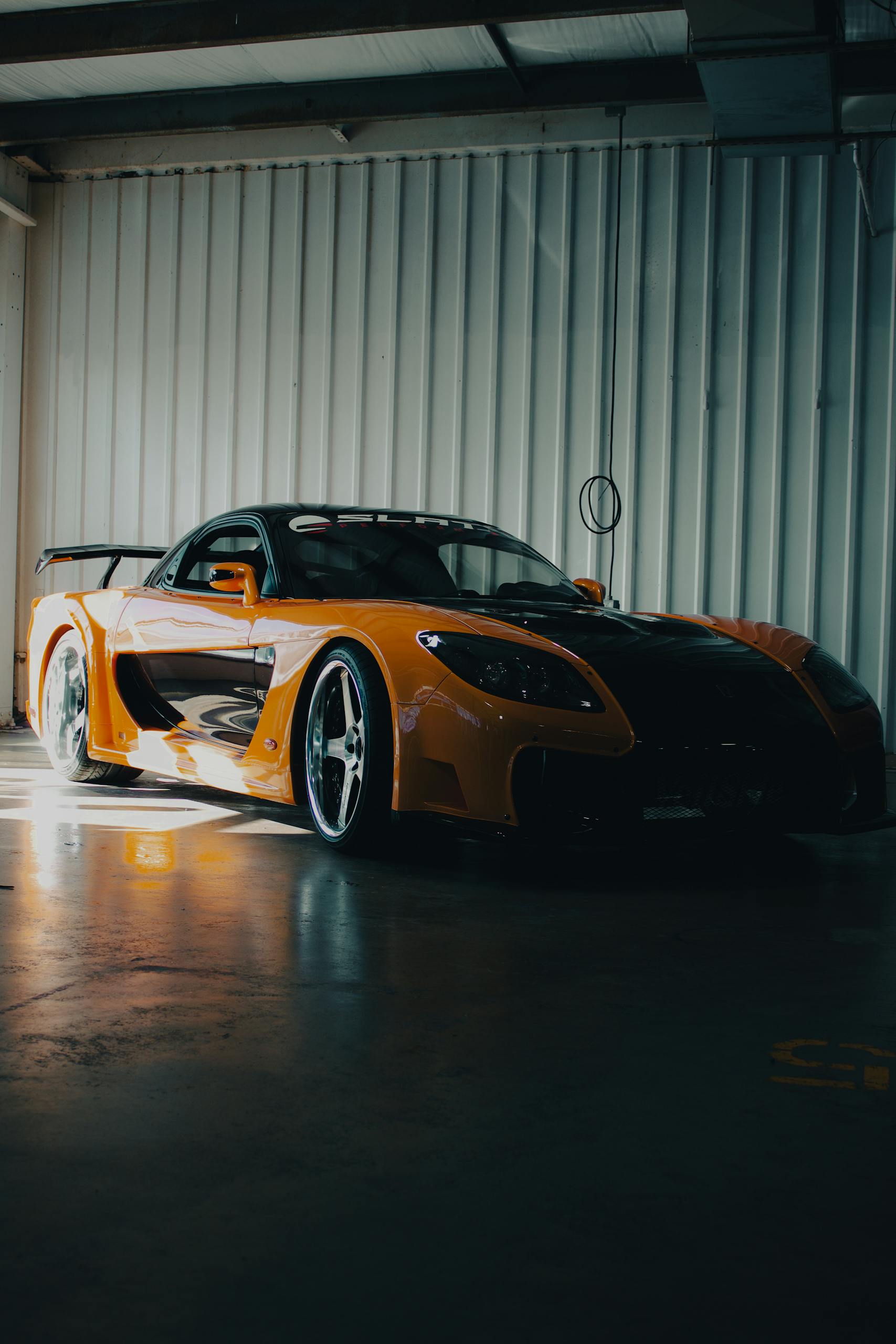 A modified Mazda RX-7 with Veilside body kit, showcasing its sleek design in a dimly lit garage.