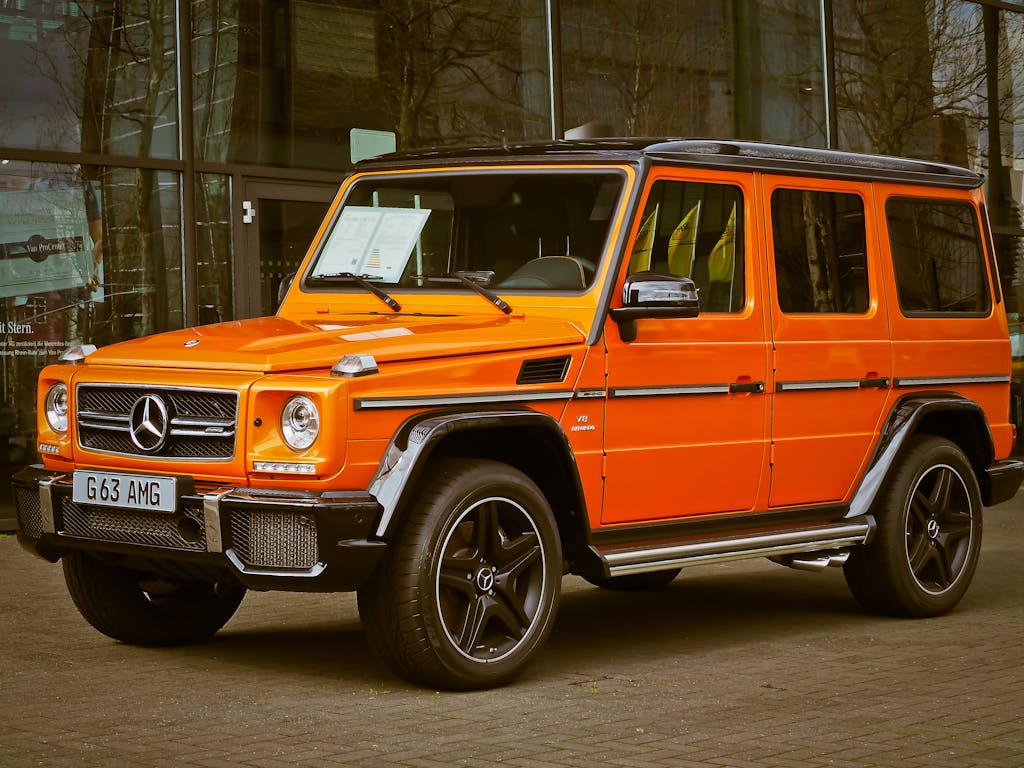 Bright orange Mercedes-Benz G Wagon parked in front of a building, showcasing luxury and style.